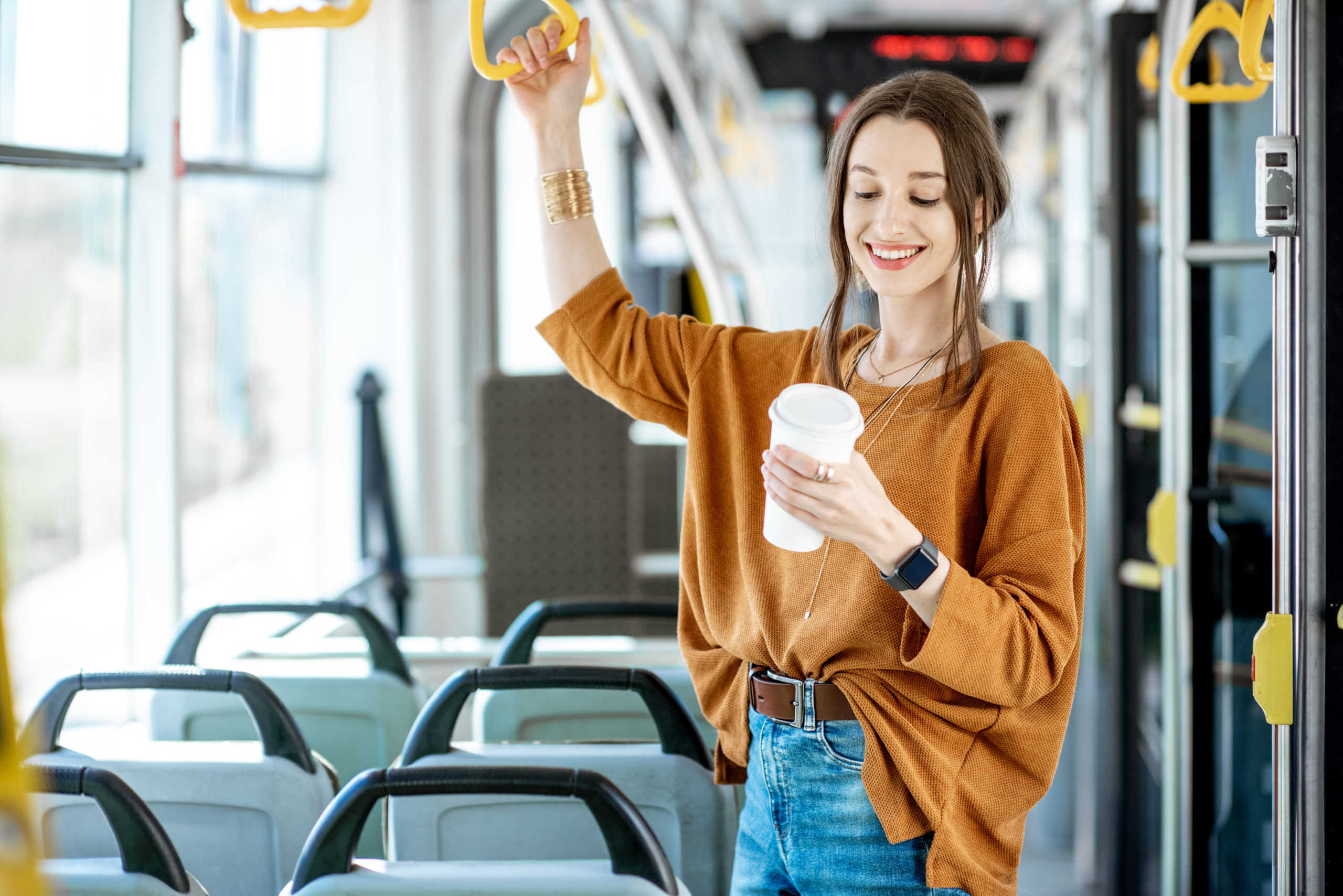 Frau im Bus, hält sich an Griff fest mit einem Kaffeebecher in der Hand
